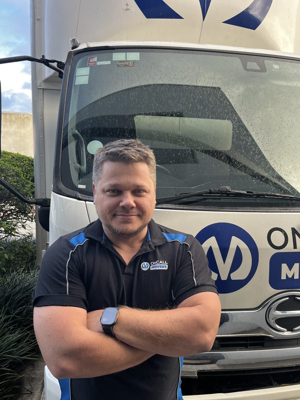 Vitali Masnyi, founder and director of OnCall Movers, standing in front of a branded OnCall Movers truck